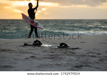 Kitesurfing board placing on the sandy beach with defocused beautiful silhouette picture of amateur female kitesurfer holding kitesurfing board bar part sling surfing board equipment prior riding wave