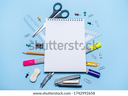 School supplies on a blue background. Back to school! Top view: school supplies are under the notebook