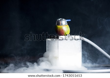 Fashionable hookah with mango, on a black background with smoke and coal. Hookah bowl of mango inside the fruit in the form of an unusual fruit hookah.