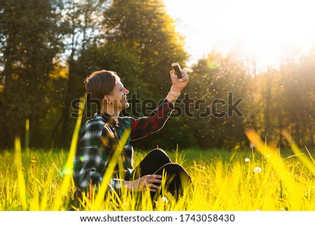 A happy young man taking a selfie on mobile phone outdoors, have a rest in summer park. Nature green background