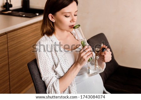 pregnant woman holding lighter near bong with legal cannabis at home Royalty-Free Stock Photo #1743084074