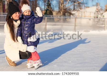 Young mother and her cute little daughter on a skating rink