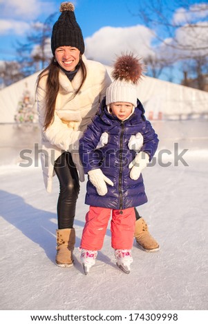 Happy adorable little girl and young mother learning ice-skating