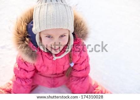 Happy adorable girl sitting on ice with skates after the fall
