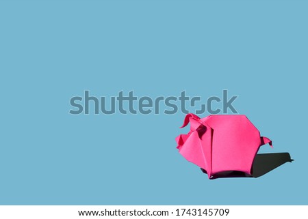 Origami pink paper pig isolated on blue background with hard shadow