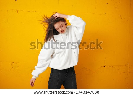 Portrait of a young pretty female student in a white hoodie, casual clothing against a concrete orange wall.