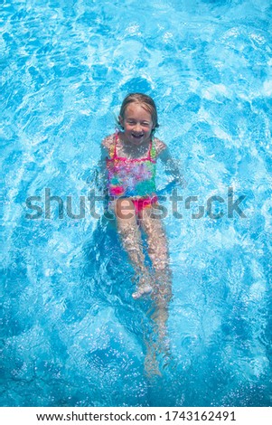 Top view of pretty young girl outdoor in the pool at the resort against blue water. Summer holiday and happy carefree childhood concept.