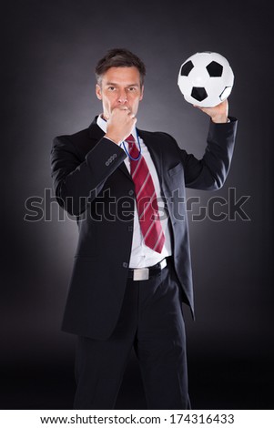 Portrait Of A Mature Businessman Holding Football Over Black Background