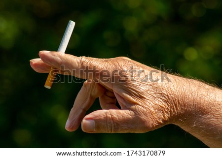 Cigarette in the hand of an old man close up, picture for design