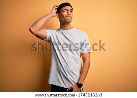 Handsome african american sportsman doing sport wearing sportswear over yellow background confuse and wondering about question. Uncertain with doubt, thinking with hand on head. Pensive concept.