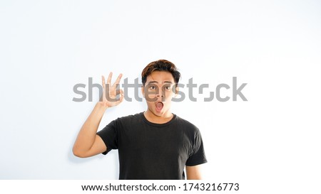 Young funny smiling handsome Asian man in casual clothes posing isolated on white background. Male sincere emotions lifestyle concept. Mock up copy space. Showing OK gesture