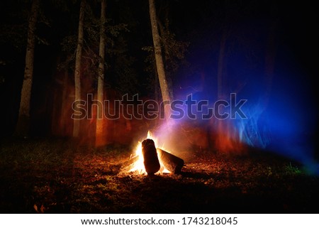 Bonfire in the mystical forest at night, tree silhouettes in the dark. Pagan traditional summer celebration in Latvia. Motion blur effect, long exposure. Eco tourism, national culture theme
