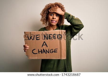 Young african american activist woman asking for change holding banner with message stressed with hand on head, shocked with shame and surprise face, angry and frustrated. Fear and upset for mistake. Royalty-Free Stock Photo #1743218687