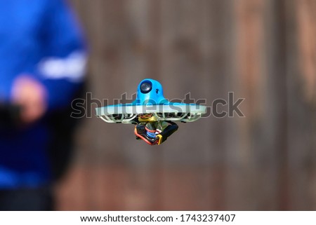 Small drone also race quad in blue is precisely controlled by the human pilot, wall in brown as background. Germany.