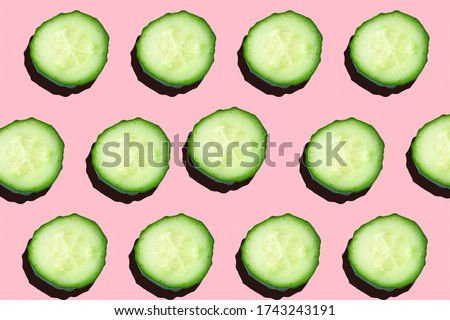 Regular seamless creative pattern of cucumber slices on a pink background.Photo collage,hard lightshadow,pop art design. Food blog, vegetable background. Printing on fabric, wrapping paper.Top view.
