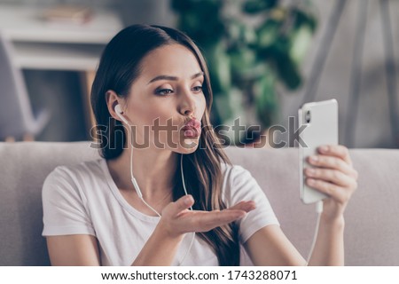Closeup photo of beautiful student lady hold telephone use earphones chatting web cam talk boyfriend send air kiss quarantine social distancing stay home sit cozy couch living room indoors