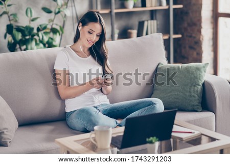 Photo of beautiful lady hold telephone notebook on table busy freelancer use earphones chatting clients customers quarantine study home sit cozy couch legs crossed living room indoors