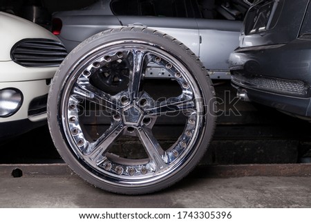 Stylish auto wheel with shiny chrome tuned disc in a repair shop between cars background for tire station or banner. Royalty-Free Stock Photo #1743305396