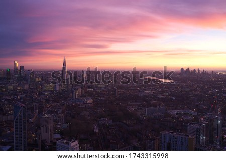 Photo shows beautiful sunrise at London where the sky is in pink and violet color. There are many houses and office building and the Thames river is reflecting the colorful sky.