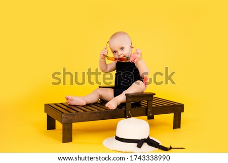 Funny little girl dressed in a red swimsuit, big hat and sunglasses heart sunbathes on a sun lounger.