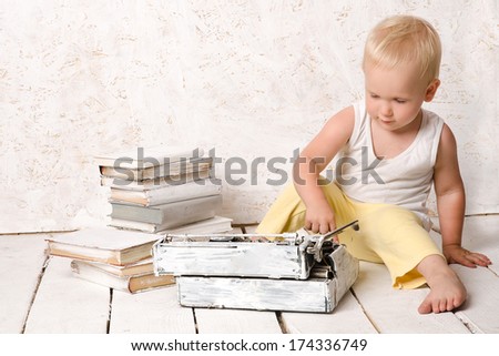 Boy sitting near retro typewriter and books on white painted floor