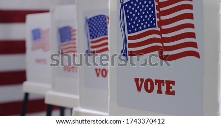 Straight on row of voting booths at polling station during American election. US flag in background. Royalty-Free Stock Photo #1743370412