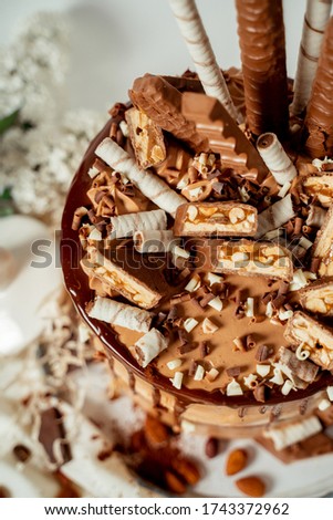 Chocolate cake decorated with various cookies and nuts on a glass plate standing on a white cloth. Food photography. Advertising and commercial close up design