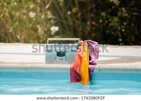 Metal radio cassette with an lgtb flag attached to the handle on the edge of a pool
