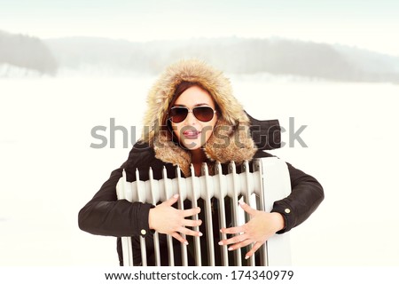 A picture of a beautiful woman hugging a radiator in winter