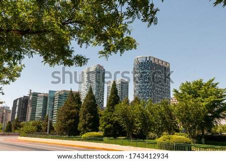 Beijing. Tall buildings against a background of green trees. Blue sky. Road without cars.