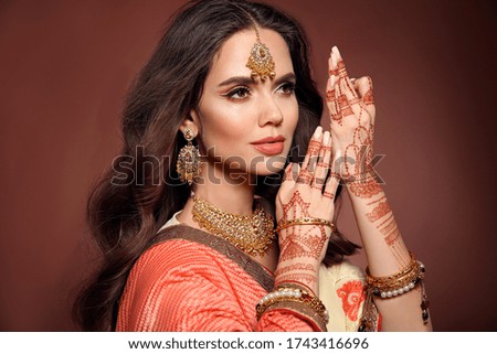 Mehendi. Portrait of beautiful indian girl in sari. Young hindu woman model with kundan golden jewelry set. Traditional Indian costume lehenga choli. Henna painting on woman's hands.