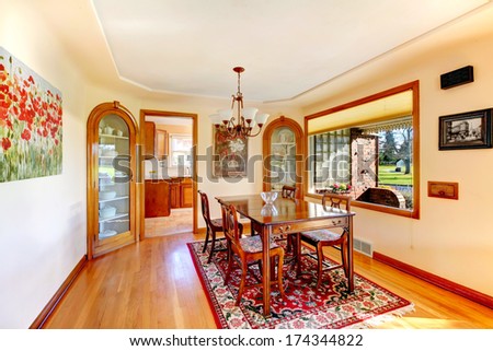Ivory dining room with big window overlooking front porch. Furnished with rustic wood table set, decorated with old style pictures