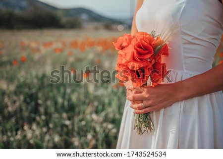 Bride in a white dress holding a bouquet of poppy flowers, warm sunset time on the background of the red poppy field. Copy space. The concept of calmness, silence and unity with nature.