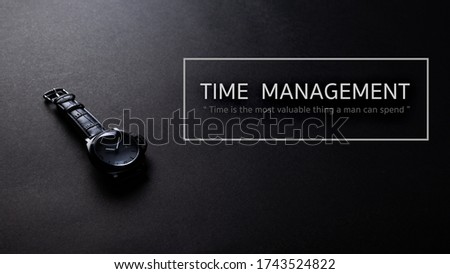 Black iron watch with black leather stap on black texture background, desk from top view, time management concept