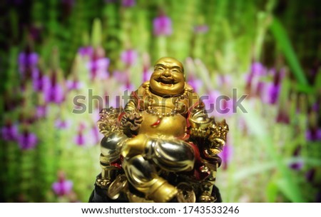 The statue of the Laughing Buddha act as a good friend. When we are off the track, his smiling face can bring us back to the present moments to a positive mood vibes. statue with violet flower garden.