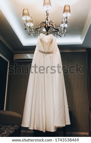 A beautiful white wedding dress of the bride hangs on a large chandelier in the interior. Photography, concept.