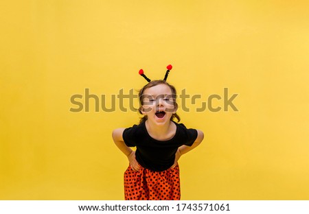 A laughing girl in a ladybug costume on a yellow isolated background with space for text.