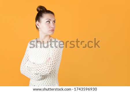 girl with resentment looks at someone over her shoulder, hands clasped on her chest. Isolated on orange-yellow background Royalty-Free Stock Photo #1743596930
