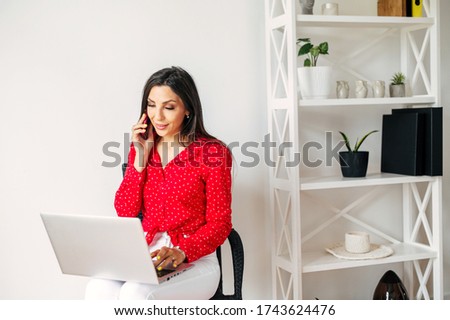 Business woman calling and working on a computer. Young girl talks via phone and using her laptop at home. Distance working from home, calling and emailing