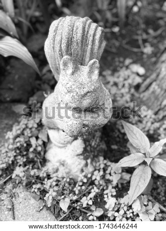 Cement squirrel sitting in a flowerbed