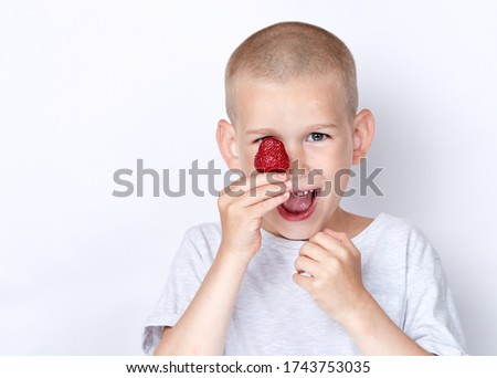 Cute cheerful child eats strawberries on a light background with free text copy space. The boy is laughing and indulges. Happy childhood concept. 
Boy in a gray shirt smiles and eats.