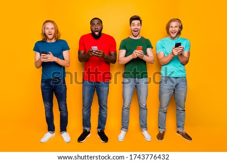 Full size photo of excited surprised four men use smartphone impressed social media news comment share post wear t-shirt denim jeans isolated over bright shine color background