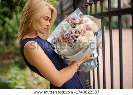 Young beautiful blond woman holds bouquet with tender spring fresh flowers in pastel colors in her hands and looks at it