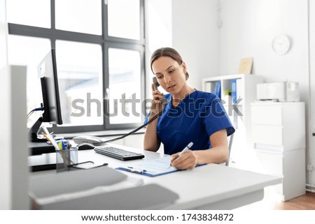 medicine, technology and healthcare concept - female doctor or nurse with computer and clipboard calling on phone at hospital