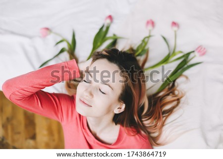 Hairstyle with flowers. Romantic portrait of a girl in bed with natural flowers. Dreamy cute young woman with tulips in hair. Beautiful fashion photo