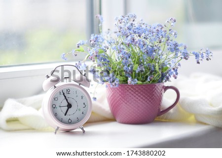 spring bouquet of flowers and a cozy white plaid on the windowsill. pink clock by the window shows morning time