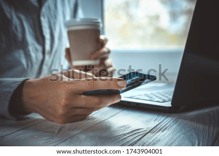 Hands with smartphone. Modern work place at home with black notebook on light window background