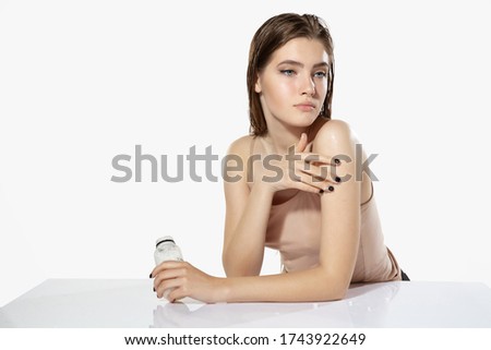 Portrait of beautiful young woman with moisturizer on white background. Concept of cosmetics, makeup, natural and eco treatment, skin care. Shiny and healthy skin, fashion, healthcare.