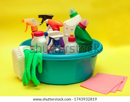 Cleaning. Bottles with cleaning products and detergents in a blue basin on a yellow background. Cleaning, disinfection. Sanitation. Space for text.