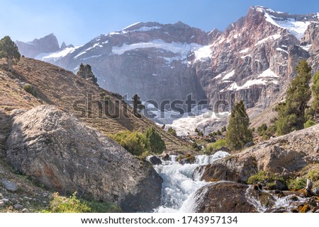 The beautiful mountain trekking road with clear blue sky and rocky hills and fresh mountain stream in Fann mountains in Tajikistan